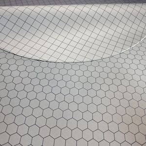 May include: A white fabric sheet featuring a black hexagonal honeycomb pattern. The top portion of the fabric is folded over, revealing a secondary layer with a black diamond grid pattern printed on a white background, creating a geometric contrast.
