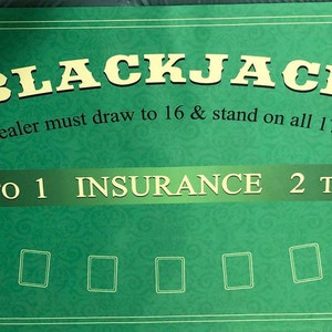 May include: A green Blackjack table with gold lettering and a decorative border. The table features the word "BLACKJACK", along with text indicating game rules and payouts. The table has spaces for players' cards.