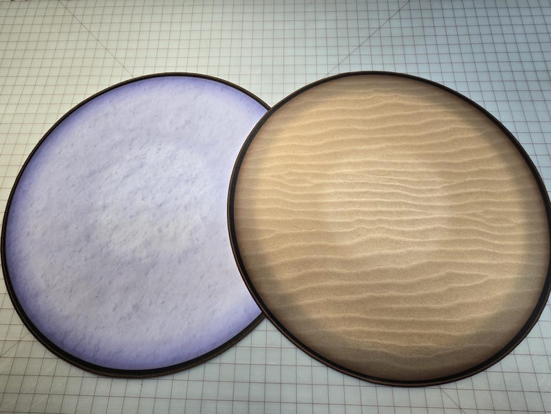 Peut inclure: Deux plateaux ronds en bois plats avec un bord noir. Un plateau a une surface marbr&eacute;e violet clair et l'autre a une surface en bois brun clair.