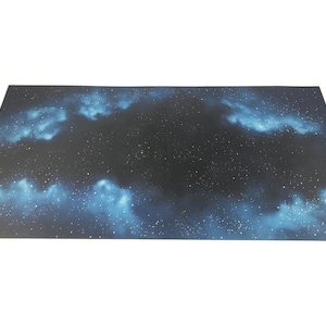 Puede incluir: Una alfombra de juego de color azul oscuro y negro con temática espacial con estrellas blancas y nebulosas azules.