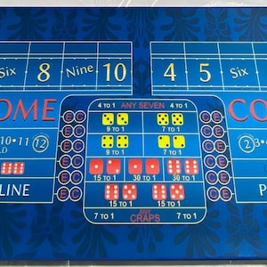 May include: A blue felt craps table with a layout for playing the game. The table has two betting areas, each with a 'Come' and 'Pass Line' area. The table also has a 'Don't Come' and 'Don't Pass Line' area. The table has a 'Craps' label in the center.
