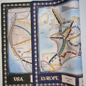 Peut inclure: Tapis de jeu de société avec des cartes des États-Unis et de l'Europe. La carte des États-Unis est verte avec "USA" en bas. La carte de l'Europe est bleue avec "EUROPE". Les deux cartes montrent des itinéraires et des noms de villes.