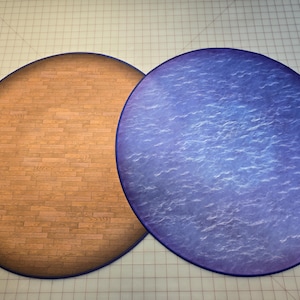 Peut inclure: Deux tapis de jeu ronds, &agrave; dos en feutre. Un tapis est brun avec un motif en bois, l'autre est bleu avec un motif de vagues.