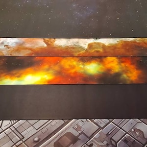 May include: Four different space-themed tablecloths rolled up on a table. The tablecloths feature a black background with white stars, a nebula with orange, red, and yellow colours, a black background with white stars, and a detailed spaceship design.