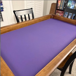 May include: A wooden game table with a purple playing surface. The table has a dark wood frame and is surrounded by black chairs. The table is designed for board games and card games.