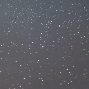 Puede incluir: Primer plano de una superficie gris con un patrón disperso de pequeños puntos blancos brillantes.