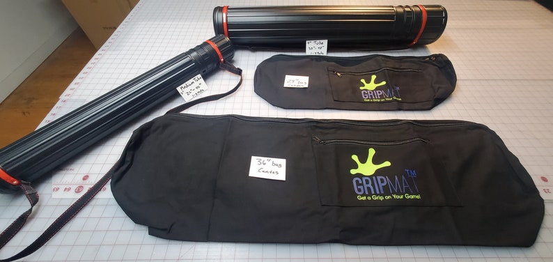 May include: Three black canvas bags with red straps and a green logo that says "Gripmat Get a Grip on Your Game". Two black tubes with red caps and labels that say "Medium Tube 21" x 36" 3200" and "36" Tube 36" x 48" 3200".