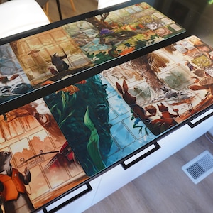 May include: Four different illustrated game mats with a grid pattern. The mats feature various scenes with animals, plants, and landscapes. The mats are made of a durable material and are perfect for use with board games or card games.