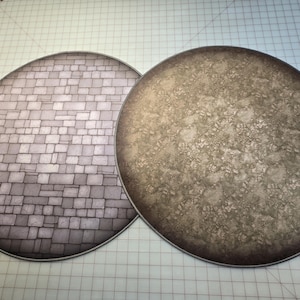 Peut inclure: Deux tapis de jeu ronds, plats et circulaires. Un tapis est de couleur gris clair avec un motif de pierre. L'autre tapis est de couleur marron avec un motif marbr&eacute;.