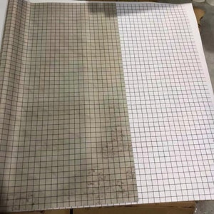 May include: A roll of white gridded paper with a section of the paper rolled up to reveal a similar gridded paper with a brown, textured surface.