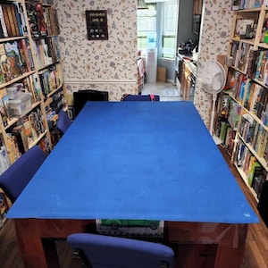 May include: A blue table top with a wooden frame and four chairs. The table is covered with a blue felt table cloth. The table is in a room with bookshelves on either side.