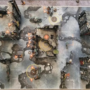 Puede incluir: Vista aérea de una mesa de juego de guerra. El tablero es gris con un patrón texturizado y presenta edificios en miniatura, terreno y figuras. Se colocan marcadores naranjas y zonas circulares en todo el tablero.