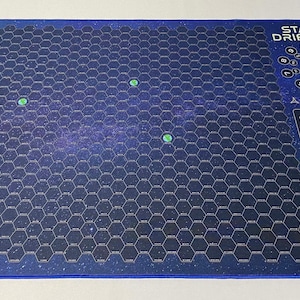 May include: A blue and white game mat with a hexagonal grid pattern and the text "STAR DRIFTER" and "STAR POINTS". There are three green circles on the mat.