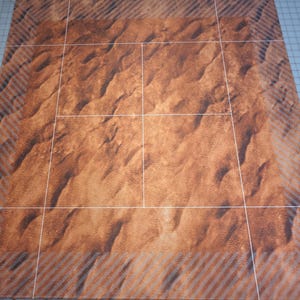 Könnte beinhalten: Eine rechteckige Matte mit einem hochauflösenden Druck von Wüstensanddünen. Das Design umfasst ein zentrales Gittermuster aus dünnen weißen Linien, umgeben von einem Rand mit einem diagonalen Streifenmuster in Braun- und Beigetönen.