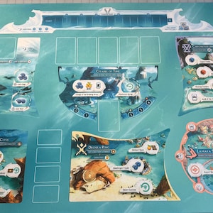 May include: A teal board game mat with various illustrated locations and spaces. The mat features detailed artwork of islands, water, and structures. The game board includes spaces for cards and tokens, with text labels and icons.
