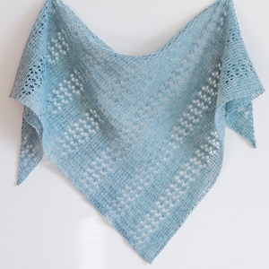 Könnte beinhalten: Hellblaues, dreieckiges Tuch mit filigranem Lochmuster. Das Tuch, vermutlich gestrickt oder gehäkelt, wird vor einem weißen Hintergrund präsentiert. Das Design umfasst geometrische Formen und einen Spitzenrand. Die Textur deutet auf ein weiches, leichtes Material hin.