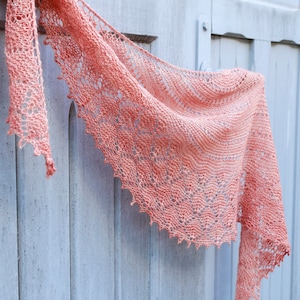 May include: A delicate peach-coloured crocheted shawl hangs on a light blue wooden door. The shawl is made with a lacy pattern and has a fringed edge.