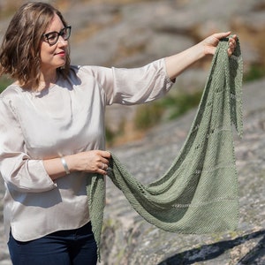 以下が含まれることがあります： 薄いベージュのトップスと青いジーンズを着用した女性が、レース模様の緑色のニットのショールを持っています。