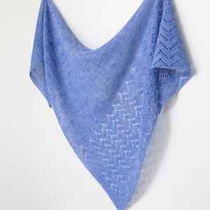 May include: A light blue knitted shawl with a lacy pattern. The shawl is hanging on a white wall.