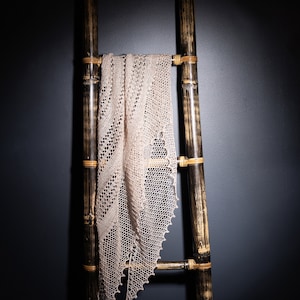 May include: A delicate, cream-colored lace shawl draped over a black bamboo ladder.