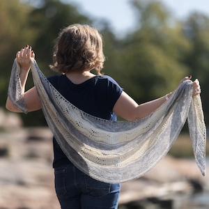 May include: A person wearing a blue shirt and jeans is holding a white and blue knitted shawl. The shawl has a lacy pattern and is draped over the person's shoulders.