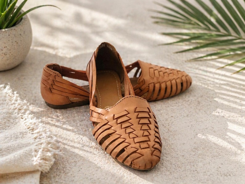 May include: A pair of tan leather huarache sandals featuring a woven lattice design across the upper, a closed rounded toe, and an open heel construction with a flat sole. The leather has a matte finish and a natural light brown color.