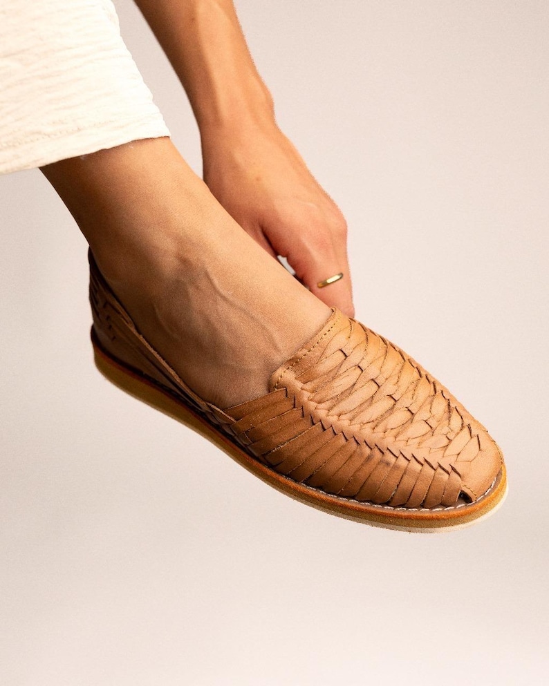 Peut inclure: Une chaussure huarache beige dot&eacute;e d'une tige en cuir tress&eacute; avec un bout ferm&eacute; et une semelle plate. La chaussure pr&eacute;sente un style &agrave; enfiler avec des bandes de cuir entrelac&eacute;es formant un motif textur&eacute; sur le dessus et les c&ocirc;t&eacute;s.