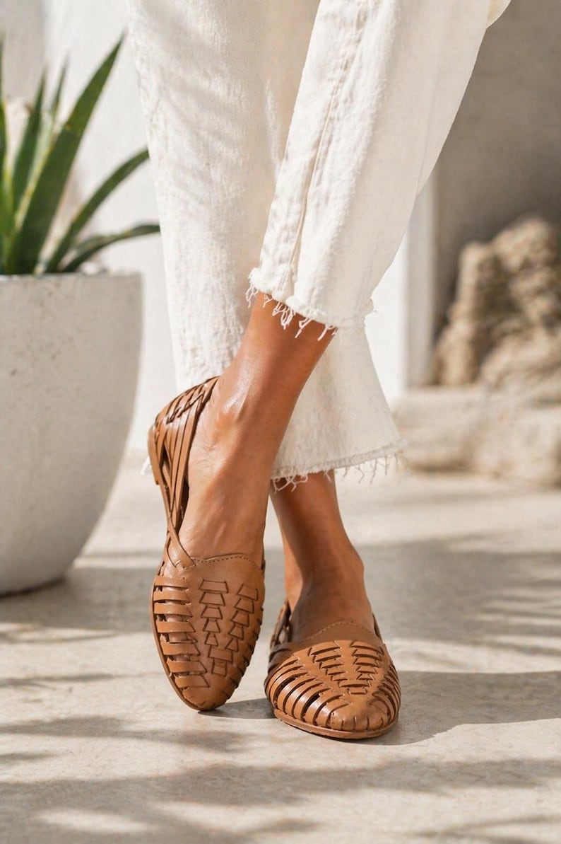 May include: A pair of tan leather huarache flats featuring a woven lattice design across the upper, a closed pointed toe, and a secure heel strap. The shoes are constructed with thin, interlaced leather strips that create a breathable pattern.