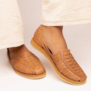 Peut inclure: Une paire de sandales huarache couleur havane dot&eacute;e d'une tige en cuir tress&eacute; avec un bout ferm&eacute; et un talon ouvert. Les chaussures pr&eacute;sentent une semelle plate de couleur claire et une conception &agrave; enfiler avec des lani&egrave;res tress&eacute;es.