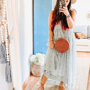 Puede incluir: Un vestido largo de color azul claro con estampado floral y silueta holgada, combinado con un sombrero de paja beige, un bolso bandolera redondo de rat&aacute;n trenzado con correa de cuero marr&oacute;n y sandalias huarache de cuero beige.