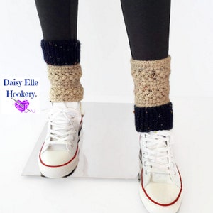 May include: Crocheted leg warmers in beige and navy blue with a speckled texture. The leg warmers are worn over black leggings and white sneakers.