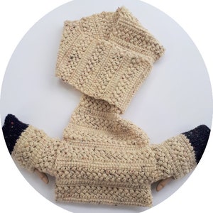May include: A beige crocheted sweater with a cowl neck and long sleeves. The sweater has a textured stitch pattern and a black and white trim on the sleeves.