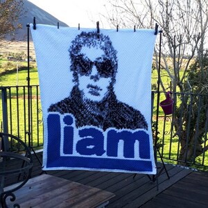 May include: A white crocheted blanket with a black and white image of a person wearing sunglasses. The name "liam" is written in blue letters at the bottom of the blanket.