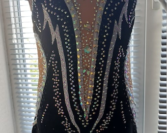 May include: Black leotard with a white and silver design and rhinestones. The leotard has a scoop neck and short sleeves.