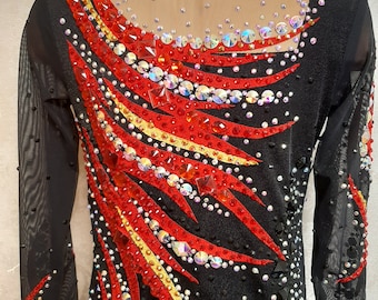Puede incluir: Leotardo negro de manga larga con un diseño rojo, dorado y negro. El diseño presenta pedrería y tiene la forma de una llama.
