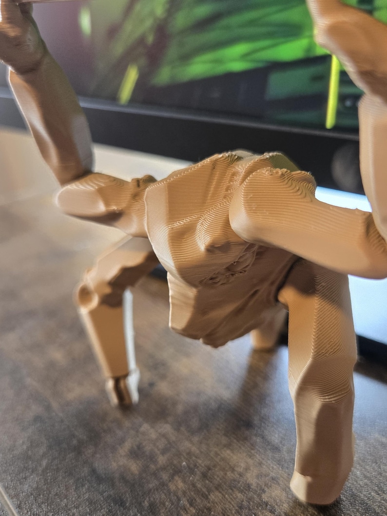 May include: A light tan, 3D-printed articulated figure with a humanoid torso and multiple limbs. The surface displays visible horizontal layer lines characteristic of additive manufacturing, with jointed segments allowing for various poses.