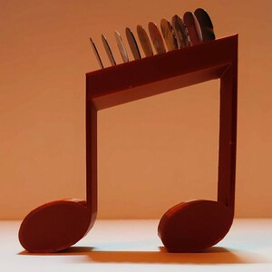 Puede incluir: Un soporte para m&uacute;sica de pl&aacute;stico rojo en forma de nota musical con una fila de discos redondos en la parte superior. El soporte est&aacute; dise&ntilde;ado para sostener y exhibir objetos peque&ntilde;os.