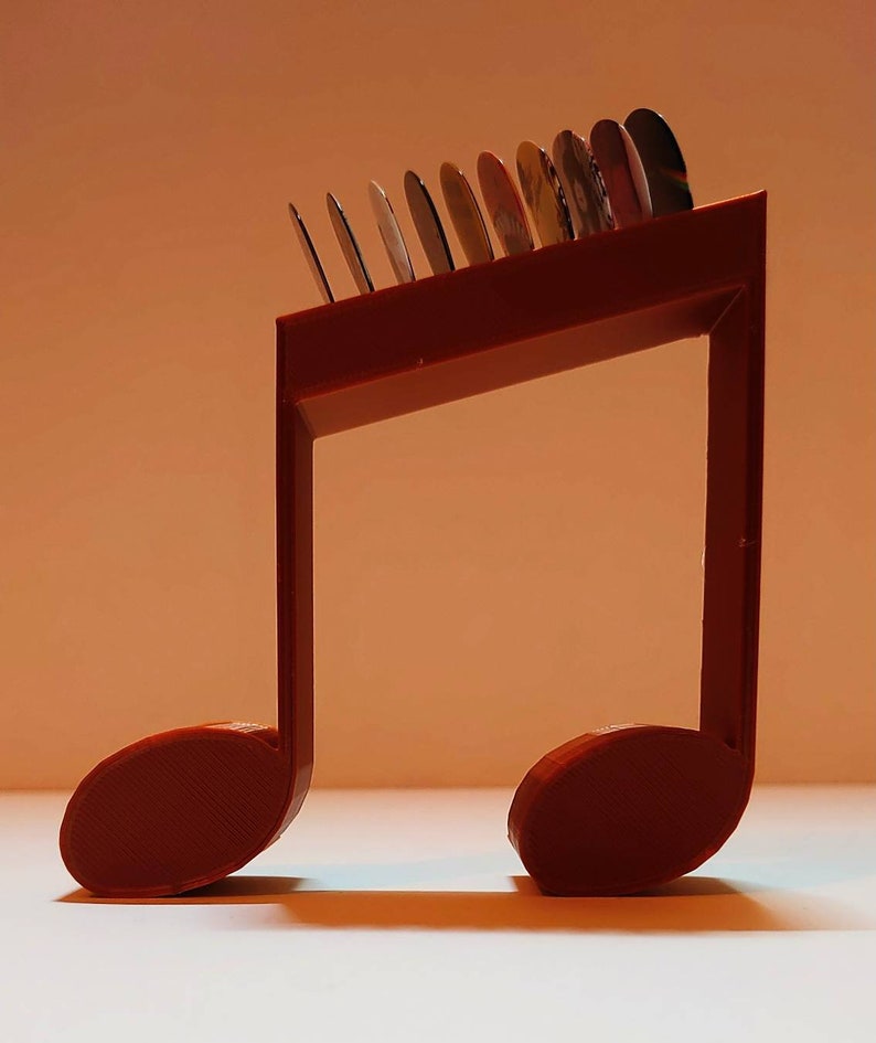 Puede incluir: Un soporte para m&uacute;sica de pl&aacute;stico rojo en forma de nota musical con una fila de discos redondos en la parte superior. El soporte est&aacute; dise&ntilde;ado para sostener y exhibir objetos peque&ntilde;os.