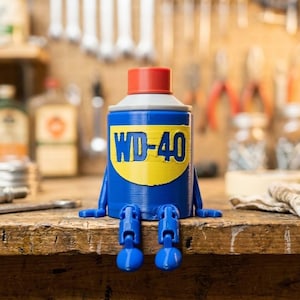 May include: A blue cylindrical figurine shaped like a spray can with a red cap and a yellow label featuring the text WD-40 in blue. The figurine has articulated blue arms and legs extending from the sides and base, allowing it to sit on an edge.