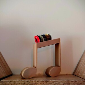 Puede incluir: Un soporte de madera para p&uacute;as de guitarra con forma de nota musical. El soporte es marr&oacute;n y tiene algunas p&uacute;as de guitarra en &eacute;l.