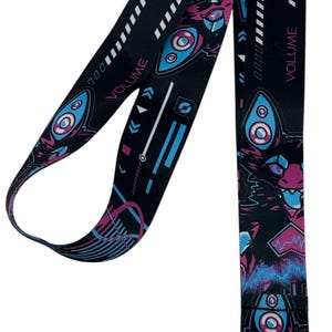 May include: Black lanyard with a repeating pattern of geometric shapes, speakers, and the word "VOLUME" in white. The design incorporates pink, blue, and white accents. A silver metal clasp is attached.