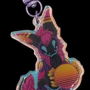 May include: A colorful acrylic keychain featuring a stylized anthropomorphic character with a black face, pink fur, and purple and yellow accents. The character is holding a sunset-themed orb. The keychain has a silver clasp.