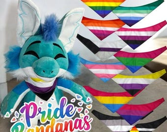 May include: A blue plush toy with a smiling face wearing a purple and black bandana. The toy is surrounded by ten different colored bandanas with various pride flag designs. The text "Pride Bandanas" is written on the bottom of the image.