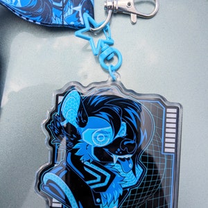 May include: A blue and black character with a blue glowing eye and tongue sticking out is printed on a clear acrylic keychain. The keychain is attached to a blue star charm and a silver chain.