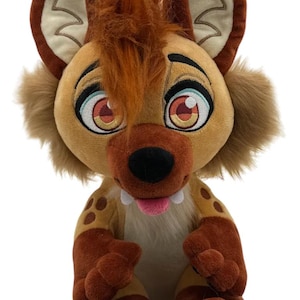 May include: A plush hyena toy with large eyes, a brown snout, and a pink tongue. The toy has brown and tan fur, with darker brown spots and paws. The ears are brown with a lighter tan interior.