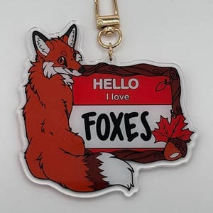 May include: A red fox keychain with a wooden frame and the text "HELLO I love FOXES". The frame has a brown maple leaf and an acorn.
