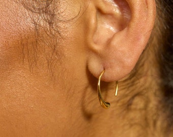 May include: A small, polished gold hoop earring with a teardrop-shaped end. The earring features a smooth, curved design that tapers to a rounded point, creating a minimalist and elegant look. The metal has a bright, reflective finish.