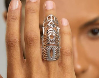 May include: A silver-toned full-finger ring featuring an intricate openwork design. The metal band covers the length of the finger with symmetrical cutouts, including a central sunburst pattern and an eye-shaped motif at the top section.