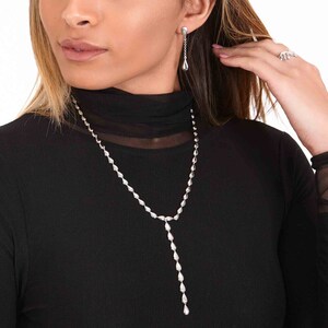 May include: A silver teardrop necklace with a long pendant and matching teardrop earrings.