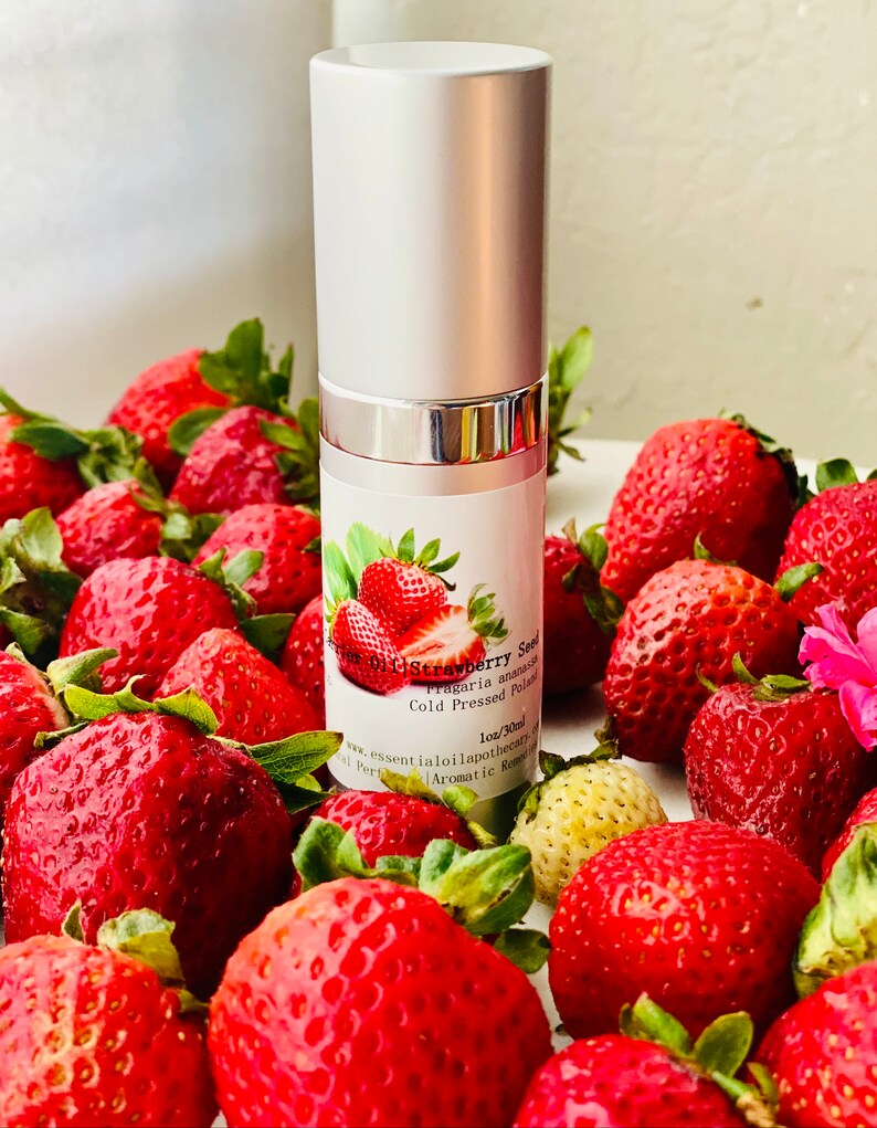 May include: A silver and white essential oil bottle labeled "Strawberry Seed" with a strawberry illustration, surrounded by fresh, ripe strawberries. The bottle is 1oz/30ml and the strawberries are a vibrant red.